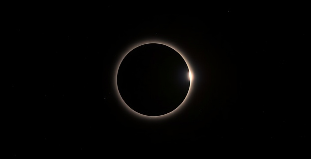 Representación de un eclipse total de Sol con la Luna pasando por delante del Sol, proyectando una sombra en la Tierra, con estrellas visibles en el cielo oscuro durante el eclipse.