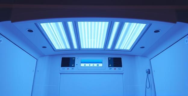 Imagen de una cabina de bronceado con luces UVA brillantes, sin personas, en un entorno clínico