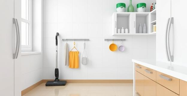 Imagen de una cocina limpia y organizada con bayetas y utensilios de limpieza ordenados, una aspiradora en un rincón y productos de limpieza en un armario cerrado.