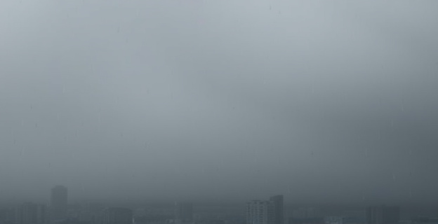 Una atmósfera densa y neblinosa, donde las gotas de agua flotan sin caer. Un cielo gris plomizo se cierne sobre un paisaje urbano o natural, pero sin signos de precipitación. El aire se siente pesado, casi palpable, y una sutil capa de humedad cubre todas las superficies. Colores apagados que transmiten una sensación de quietud tensa, con un contraste entre la pesadez del aire y la ausencia de lluvia visible.