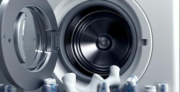 Una lavadora con la puerta abierta mostrando el tambor y el caucho donde se pueden quedar atrapados los calcetines. Alrededor, calcetines dispersos y algunos atados con clips.